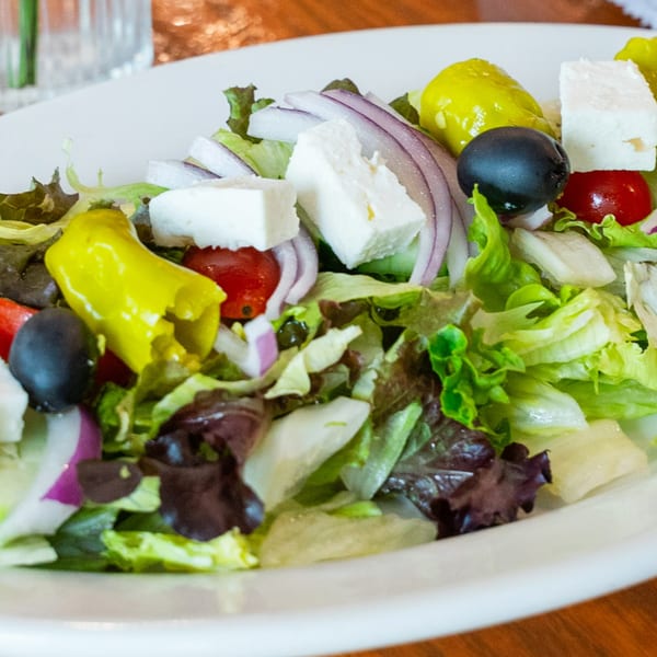 A fresh Persian salad with lettuce, red onion, feta, olives, tomatoes, and yellow peppers.
