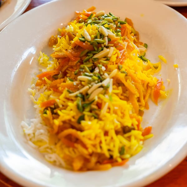 Persian rice dish with saffron, orange peel, pistachios, and almonds on a white plate.