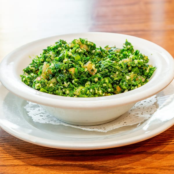 A white bowl filled with vibrant green Tabbouleh salad, featuring parsley, tomatoes, and bulgur.