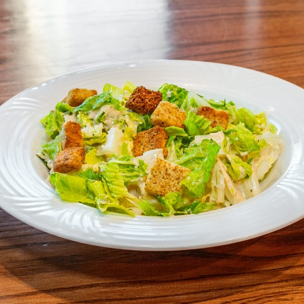 A white plate filled with fresh green Caesar salad, topped with creamy dressing and golden croutons.