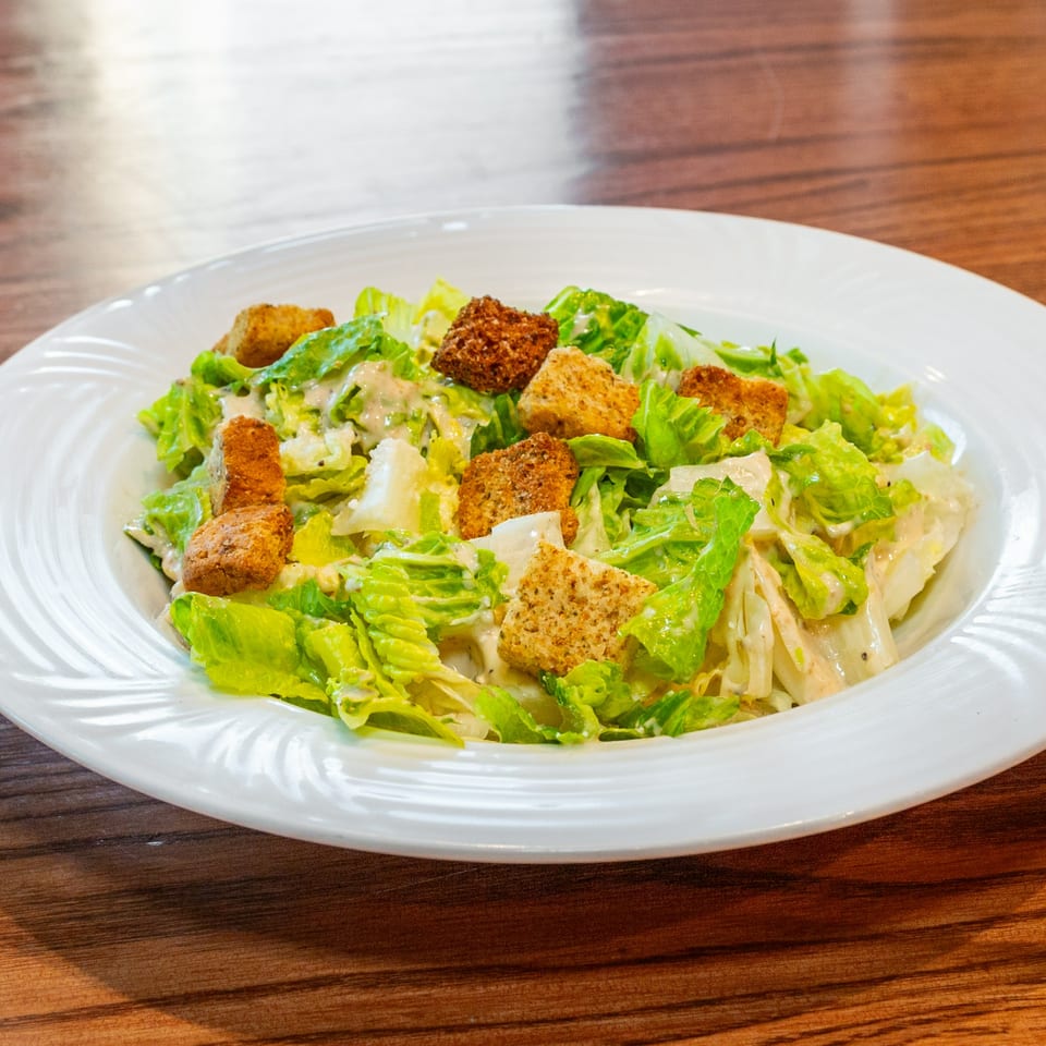 A white plate filled with fresh green Caesar salad, topped with creamy dressing and golden croutons.