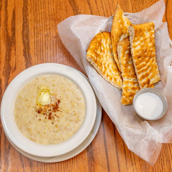 A bowl of Persian Halim with butter and cinnamon, served with flatbread and sugar.