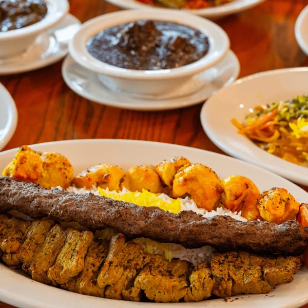 A platter of Persian kabobs with rice, alongside bowls of stews and a side dish.