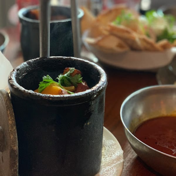 A black pot of Persian stew with herbs, next to a bowl of red soup and flatbread.