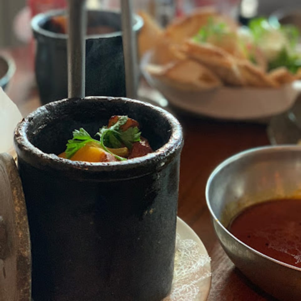 A black pot of Persian stew with herbs, next to a bowl of red soup and flatbread.