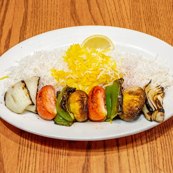 Grilled vegetable skewer with tomatoes, onions, bell peppers, and mushrooms, served with rice and lemon.